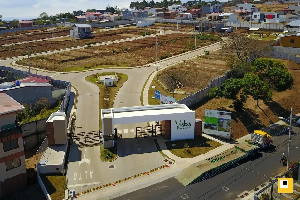 Impresionante fachada de ingreso a Vistas de San Rafael, un reflejo de la calidad de nuestra desarrolladora inmobiliaria. Vista aérea de la moderna entrada principal del condominio Vistas de San Rafael.